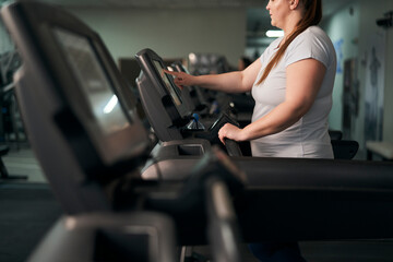 Naklejka na ściany i meble Part of plus size caucasian woman preparing for running on treadmill at gym