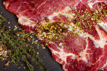Raw piece of meat with spice and sprig of thyme on the dark table close-up