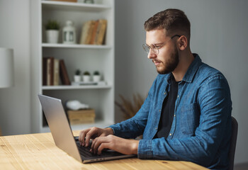 Young handsome man working on laptop at home, coding on computer remotely