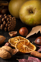 Close-up of dried orange slices on wooden table with nuts, cinnamon, apples and autumn leaves, selective focus, vertical