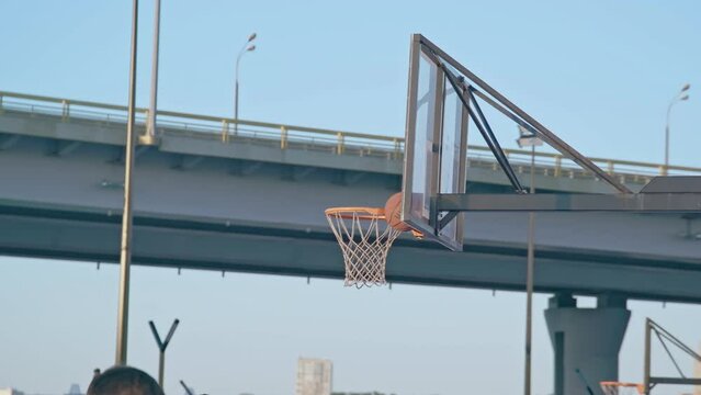 Ball stuck between shield and hoop after throw fail on sports ground against bridge. Outdoors activity in large city