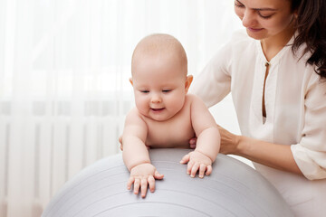 mother playing with her baby girl on a fitness ball