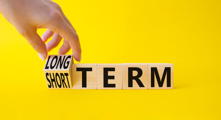Long term vs Short Term symbol. Businessman hand turnes wooden cubes and changes words Short term to Long Term. Beautiful yellow background. Business concept. Copy space.
