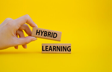Hybrid learning symbol. Concept word Hybrid learning on wooden blocks. Beautiful yellow background. Businessman hand. Business and Hybrid learning concept. Copy space