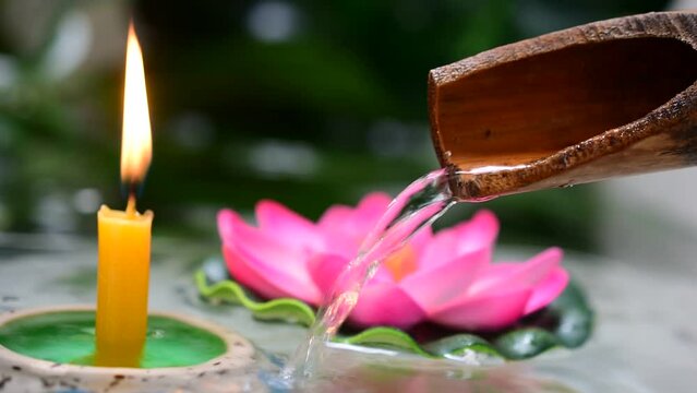 Bamboo gutter with flowing water, candle flames light up the darkness, spa concept video.