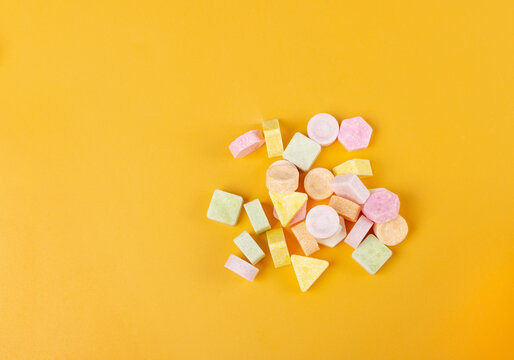 Tablet candies on yellow background. Compressed sugar powder confectionery, dextrose candy necklace parts, vitamin c tablets, lozenges pile top view