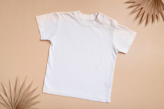 White baby t-shirt top view. Mock-up for logo, text or design on beige background. Flat lay child clothes