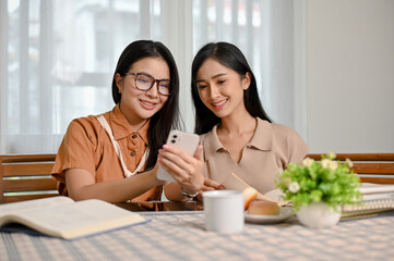 Asian female friends relaxing, looking something at smartphone screen together.