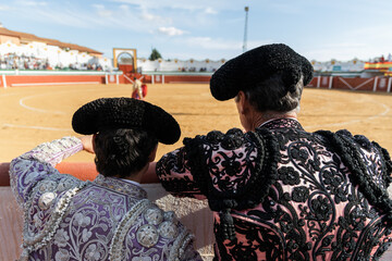 Male matadors standing behind fence of bullring