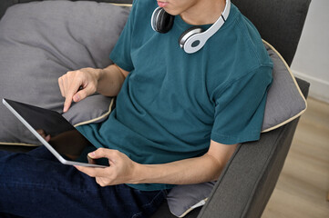 Hipster young Asian male using digital tablet touchpad while relaxing at home. cropped image