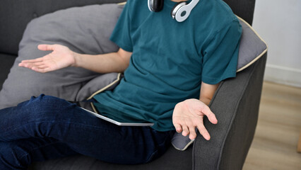 Asian male relaxing in the living room, sitting on his couch and using digital tablet.