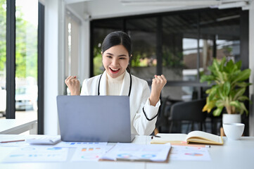 Successful Asian businesswoman celebrating at her office desk.