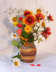 Bouquet of summer flowers in a clay vase on a light fabric background. Peaches standing in a deep plate next to each other