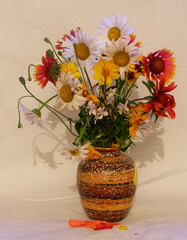 Bouquet of summer flowers in a clay vase on a light fabric background. Peaches standing in a deep plate next to each other