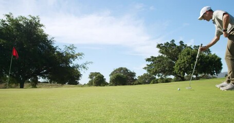 Caucasian male golfer kneeling on a golf course on a sunny day