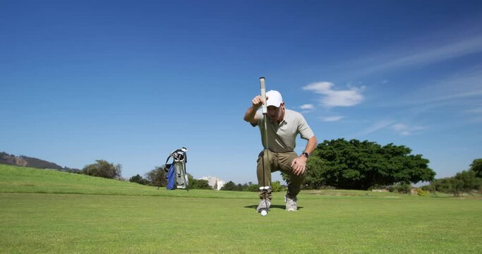 Caucasian male golfer kneeling on a golf course on a sunny day