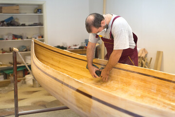 Young carpenter making wooden boat in his carpentry workshop	