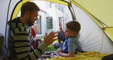 Caucasian man lying in a tent with his son in the garden talking and high fiving