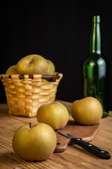 Pippin apples closeup on rustic wooden table with knife, green bottle and basket, selective focus, black background, vertical