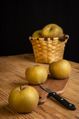 Top view of pippin apples on rustic wooden table with knife and basket, selective focus, black background, vertical
