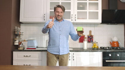 A young man is holding something green in the kitchen, showing a product, smiling and presenting a cheerful, imaginary object.  © Red Stock