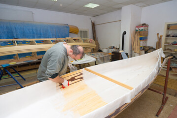 Fototapeta na wymiar Young carpenter making wooden boat of his own design in his workshop