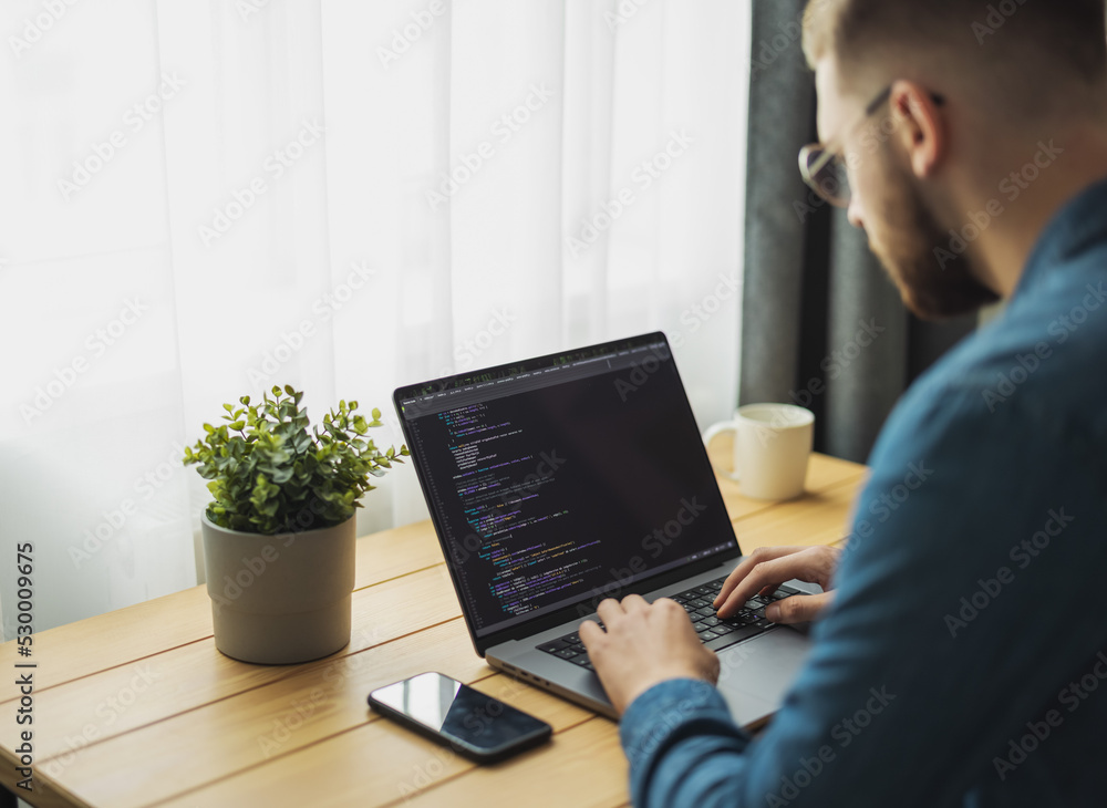 Poster man coding on laptop on a desk, remote working from home