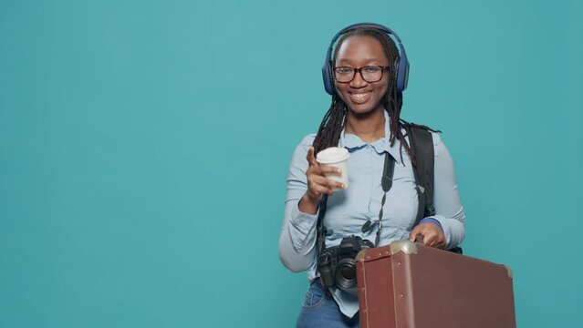 Portrait of woman carrying suitcase and backpack to go on holiday vacation trip, taking pictures with camera. Photographer with headphones drinking coffee and travelling with photography equipment.