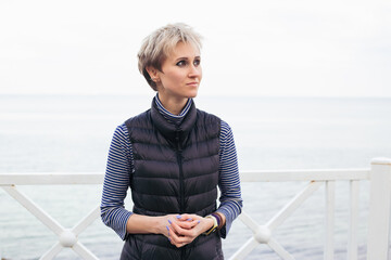 Fototapeta premium portrait of woman near sea. Female model with short hair having walk on cloudy day. Nature, spare time concept