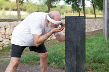 elderly man drinking water from the fountain after morning exercise in the public park