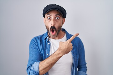 Hispanic man with beard standing over isolated background surprised pointing with finger to the...