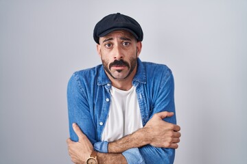 Hispanic man with beard standing over isolated background shaking and freezing for winter cold with...
