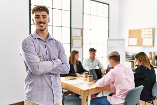 Young hispanic businessman smiling happy standing with arms crossed gesture at the office during business meeting.