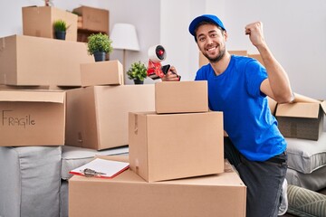Hispanic man with beard working moving boxes screaming proud, celebrating victory and success very excited with raised arms