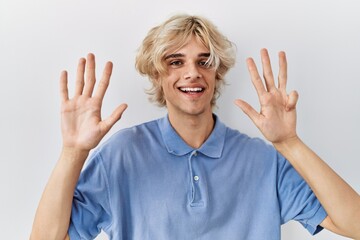 Young modern man standing over isolated background showing and pointing up with fingers number nine...