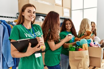 Group of young volunteers woman working at charity center. Girl smiling happy writing on clipboard.