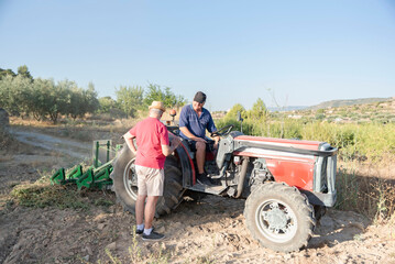 two older farmers talking in the field about a tractor problem, one of them sitting on a tractor