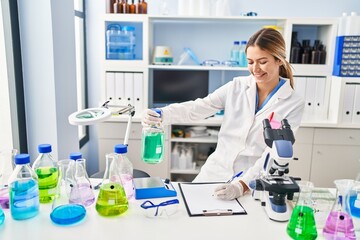 Young hispanic woman scientist measuring liquid write on document at laboratory