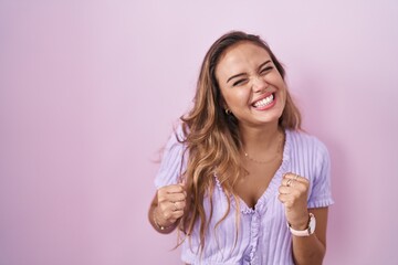 Young hispanic woman standing over pink background very happy and excited doing winner gesture with arms raised, smiling and screaming for success. celebration concept.