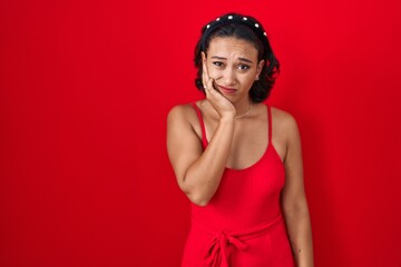 Obraz na płótnie Canvas Young hispanic woman standing over red background touching mouth with hand with painful expression because of toothache or dental illness on teeth. dentist