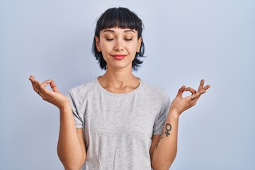 Young hispanic woman wearing casual t shirt over blue background relax and smiling with eyes closed doing meditation gesture with fingers. yoga concept.