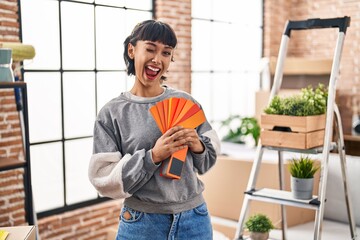 Young hispanic woman moving to a new home choosing paint winking looking at the camera with sexy...