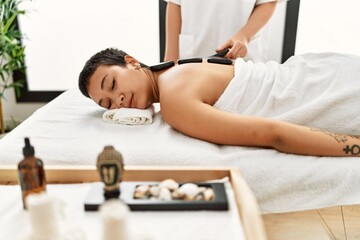 Obraz na płótnie Canvas Young hispanic woman having back massage using black hot stones at beauty center