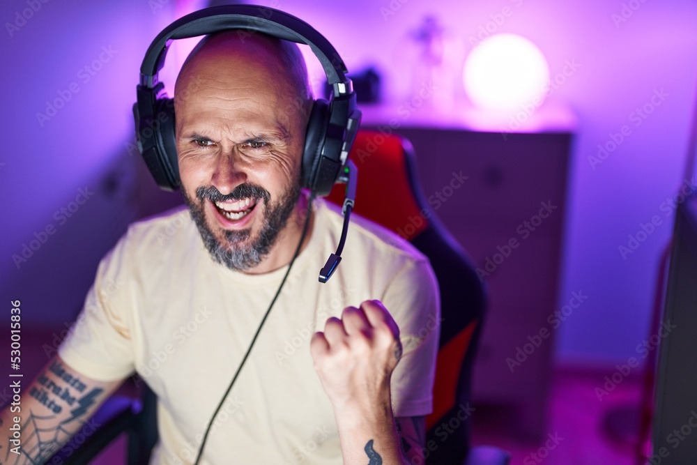 Canvas Prints Young bald man streamer playing video game with winner expression at gaming room