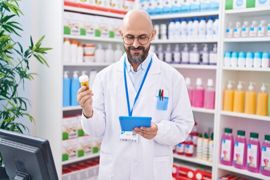 Young bald man pharmacist using touchpad holding pills bottle at pharmacy