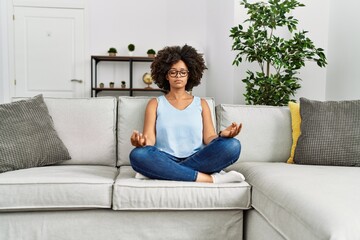 Young african american woman doing yoga sitting on sofa at home