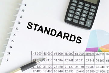 STANDARDS text on notepad on a table next to calculator, pen, reports and charts