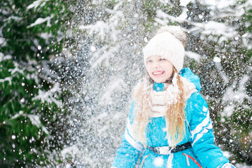 Fototapeta na wymiar A cute little girl in white hat throws up the snow.