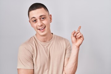 Fototapeta premium Young man standing over isolated background with a big smile on face, pointing with hand finger to the side looking at the camera.
