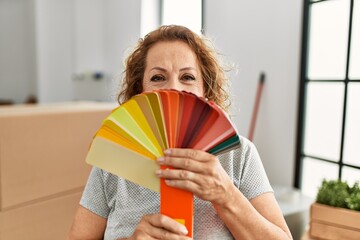 Middle age caucasian woman covering mouth with color paint test at new home.
